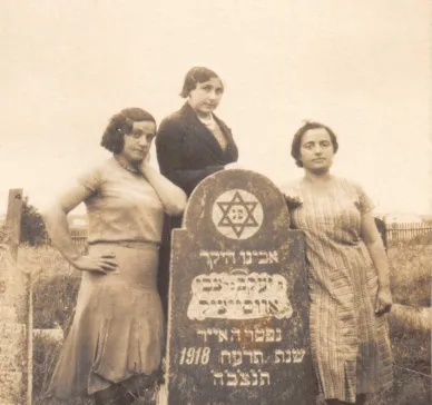 Photo of three women. They are the sisters of Harvey Sohnen’s grandmother. Rezia was a teacher, Nechama a housewife, and Lea owned a grocery. They were all murdered during the Holocaust. They stand near their father’s grave in the Jewish graveyard of Oshmyany. The photo was been taken between May 1929 and the Second World War. The inscription in Yiddish on the back of the photograph says: “Remember Father's yortsayt”. 